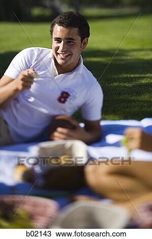 Young man lying on a picnic blanket in a park View Large Photo Image Stock Image - Young man lying on a picnic blanket in a park. Fotosearch