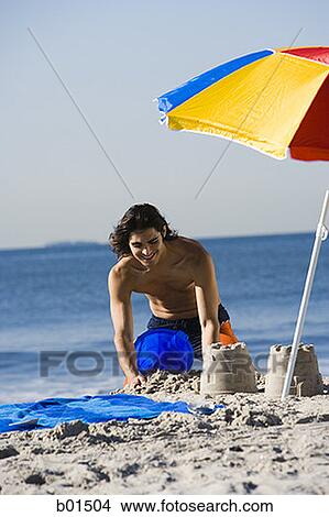 Young man making sand castle on the beach View Large Photo Image Picture - Young man making sand castle on the beach. Fotosearch