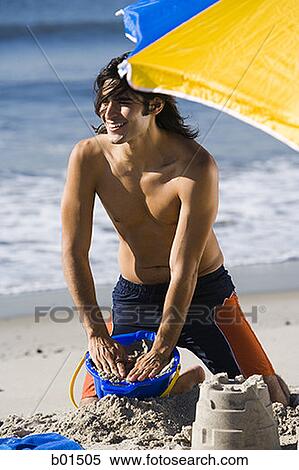 Young man making sand castle on the beach View Large Photo Image Stock Photography - Young man making sand castle on the beach. Fotosearch