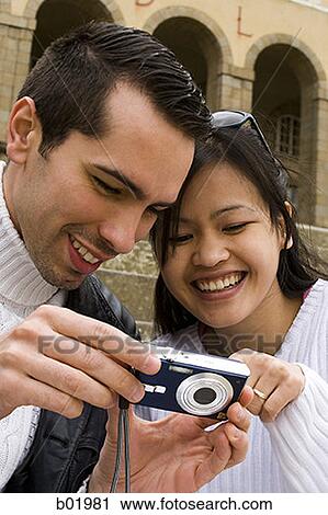 Stock Image - Young man showing a digital camera to a young woman. Fotosearch