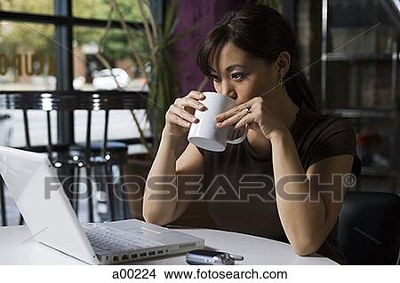 Young woman drinking coffee and working on a laptop View Large Photo Image Picture - Young woman drinking coffee and working on a laptop. Fotosearch