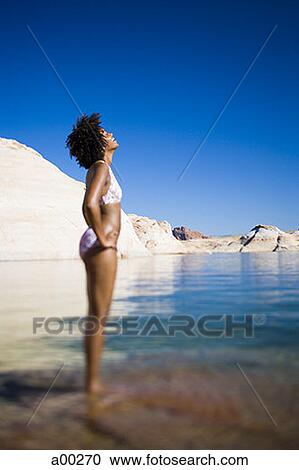 Stock Image - Young woman in a bikini and standing in water. Fotosearch