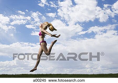 Young woman in a bikini jumping on grass View Large Photo Image Stock Photography - Young woman in a bikini jumping on grass. Fotosearch