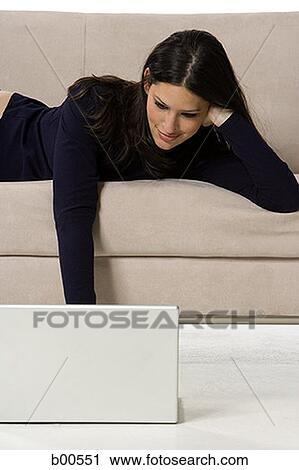 Young woman lying on a couch and using a laptop View Large Photo Image Stock Image - Young woman lying on a couch and using a laptop. Fotosearch