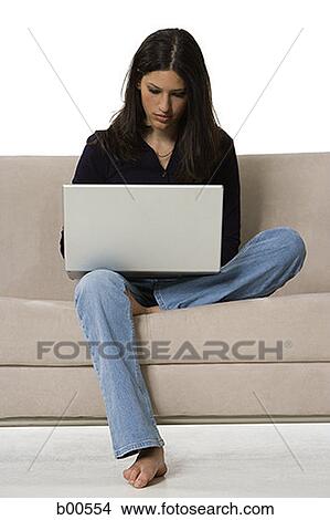 Young woman sitting on a couch and using a laptop View Large Photo Image Picture - Young woman sitting on a couch and using a laptop. Fotosearch