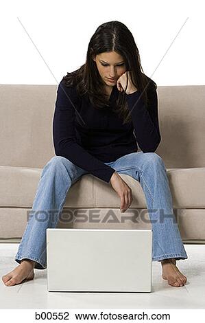 Young woman sitting on a couch and looking at a laptop View Large Photo Image Stock Image - Young woman sitting on a couch and looking at a laptop. Fotosearch