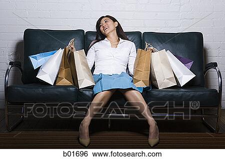 Stock Photograph - Young woman sitting on a couch with shopping bags. Fotosearch