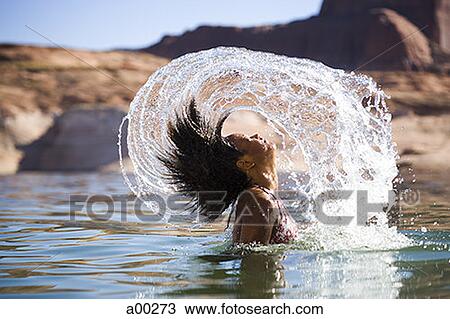 Stock Image - Young woman tossing her wet hair in a lake. Fotosearch
