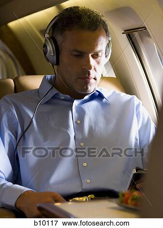 A businessman listening to music on headphones in an airplane View Large Photo Image Stock Photo - A businessman listening to music on headphones in an airplane. Fotosearch