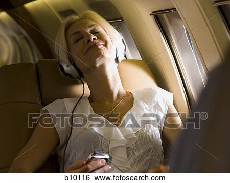 A businesswoman listening to music on headphones in an airplane View Large Photo Image Stock Photograph - A businesswoman listening to music on headphones in an airplane. Fotosearch