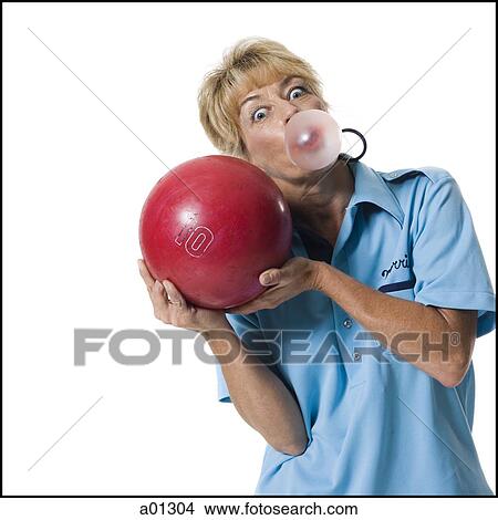 Picture - a female bowler playfully blows a bubble while holding up a ball. Fotosearch