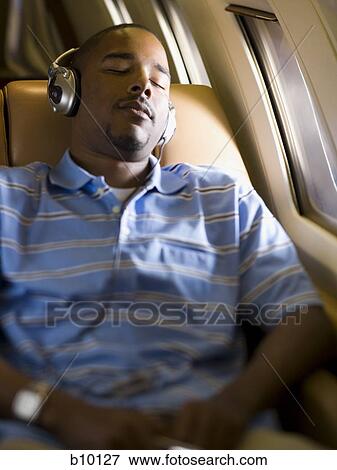 Stock Photo - A man listening to music on headphones in an airplane. Fotosearch