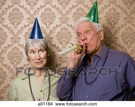 A senior man standing with a senior woman and blowing a party favor View Large Photo Image Picture - A senior man standing with a senior woman and blowing a party favor. Fotosearch