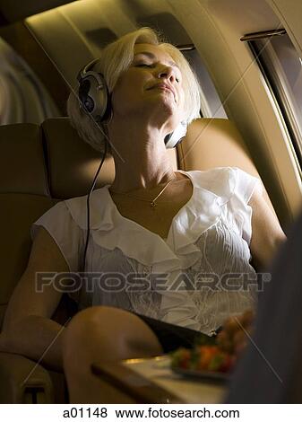 A senior woman wearing headphones and sleeping in an airplane View Large Photo Image Stock Photo - A senior woman wearing headphones and sleeping in an airplane. Fotosearch