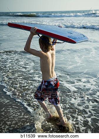 Stock Photo - Boy running at the beach with a boogie board.. Fotosearch