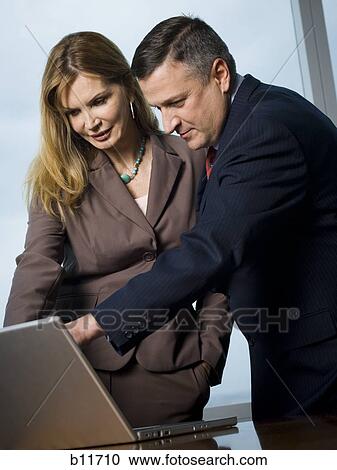 Stock Image - Businessman and businesswoman looking at laptop. Fotosearch