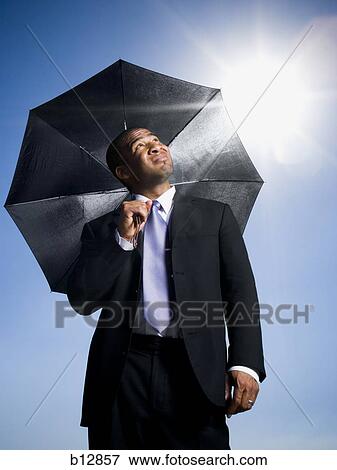 Businessman holding umbrella on a clear day View Large Photo Image Stock Photo - Businessman holding umbrella on a clear day. Fotosearch