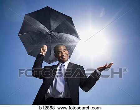 Stock Photo - Businessman holding umbrella on a clear day. Fotosearch