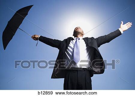 Businessman holding umbrella on a clear day View Large Photo Image Stock Photo - Businessman holding umbrella on a clear day. Fotosearch