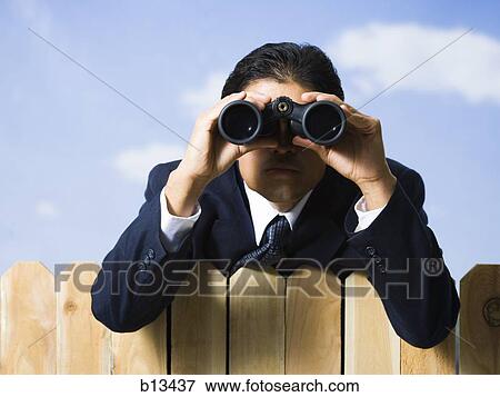 Businessman looking through binoculars over wooden fence View Large Photo Image Stock Photo - Businessman looking through binoculars over wooden fence. Fotosearch