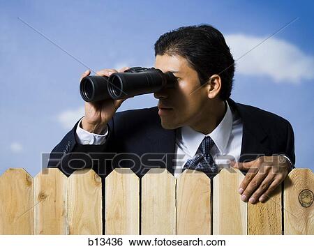Stock Photograph - Businessman looking through binoculars over wooden fence. Fotosearch