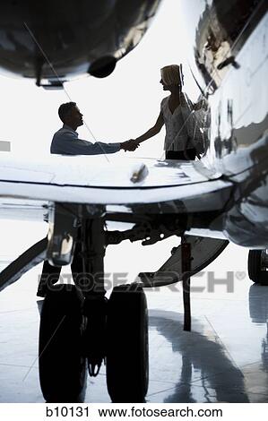 Stock Image - Businessman shaking hands with a businesswoman stepping down from an airplane. Fotosearch