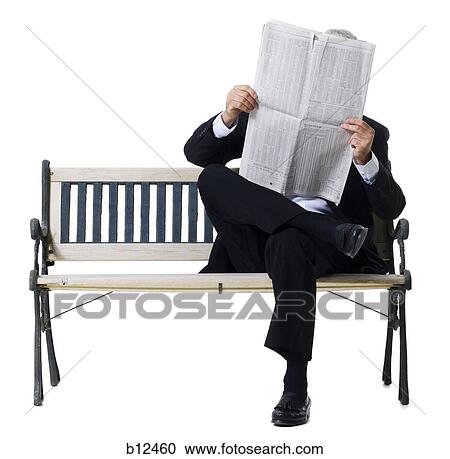 Stock Image - Businessman sitting on bench reading newspaper. Fotosearch