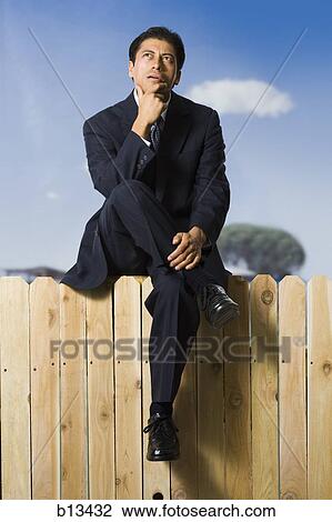 Stock Image - Businessman sitting on fence looking up. Fotosearch