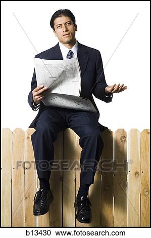 Stock Image - Businessman sitting on fence with newspaper. Fotosearch
