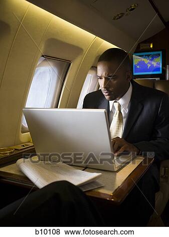 Businessman using a laptop in an airplane View Large Photo Image Stock Photo - Businessman using a laptop in an airplane. Fotosearch