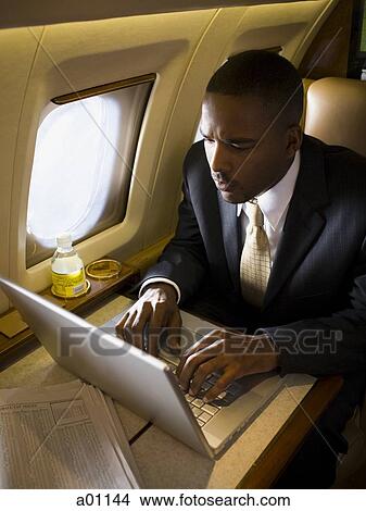 Businessman working on a laptop in an airplane View Large Photo Image Picture - Businessman working on a laptop in an airplane. Fotosearch