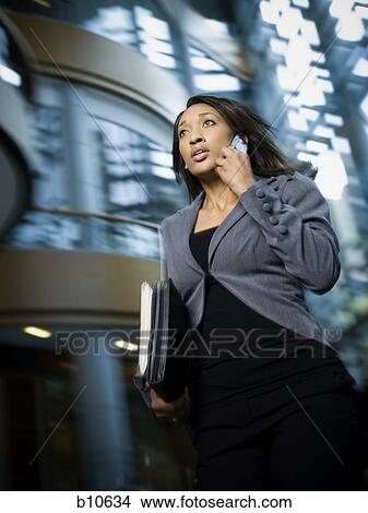 Businesswoman using a mobile phone and carrying files View Large Photo Image Picture - Businesswoman using a mobile phone and carrying files. Fotosearch