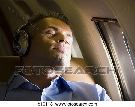 Close-up of a businessman sleeping and listening to music on headphones in an airplane View Large Photo Image Stock Photo - Close-up of a businessman sleeping and listening to music on headphones in an airplane. Fotosearch