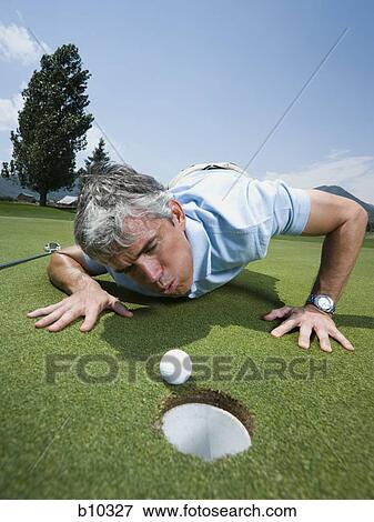 Stock Photo - Close-up of a man blowing a golf ball towards a hole. Fotosearch