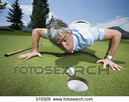 Close-up of a man blowing a golf ball towards a hole View Large Photo Image Stock Photo - Close-up of a man blowing a golf ball towards a hole. Fotosearch