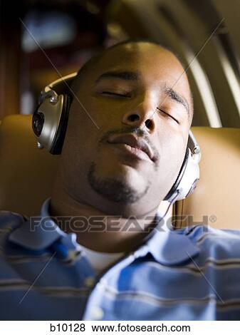 Close-up of a man listening to music on headphones in an airplane View Large Photo Image Stock Photo - Close-up of a man listening to music on headphones in an airplane. Fotosearch
