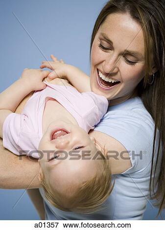 Close-up of a mother holding baby girl and laughing View Large Photo Image Stock Photo - Close-up of a mother holding baby girl and laughing. Fotosearch
