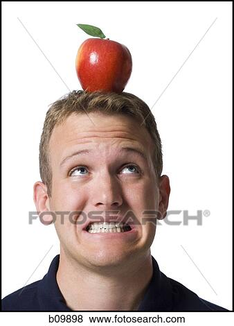 Close-up of a young man clenching his teeth with an apple on his head View Large Photo Image Stock Photo - Close-up of a young man clenching his teeth with an apple on his head. Fotosearch