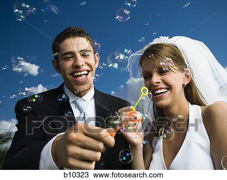 Stock Image - Close-up of newlywed couple blowing bubbles with a bubble wand. Fotosearch