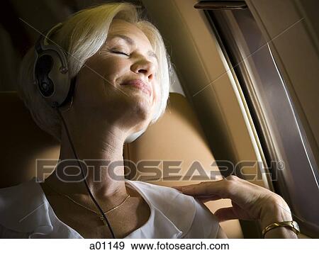 Stock Photo - Close-up of senior woman wearing headphones and sleeping in an airplane. Fotosearch