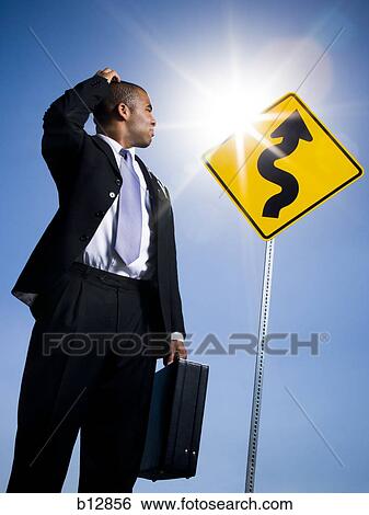Confused businessman in front of road sign View Large Photo Image Stock Photograph - Confused businessman in front of road sign. Fotosearch