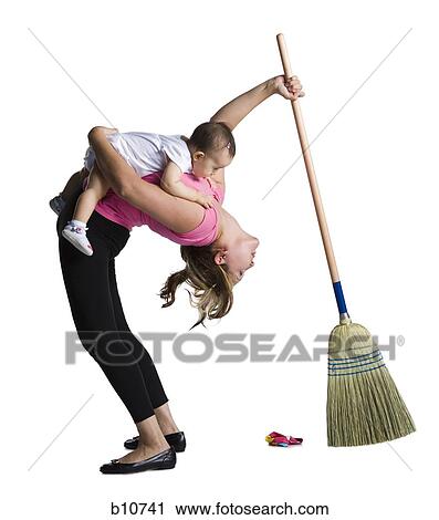 Stock Image - Contortionist mother sweeping while holding baby daughter. Fotosearch