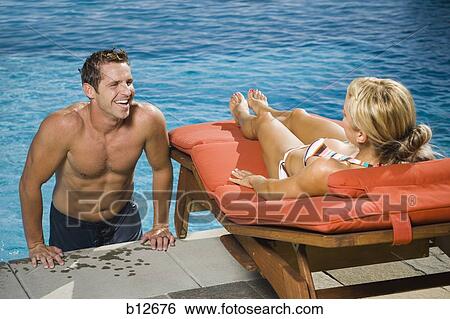 Couple in and sitting by a swimming pool View Large Photo Image Stock Photograph - Couple in and sitting by a swimming pool. Fotosearch