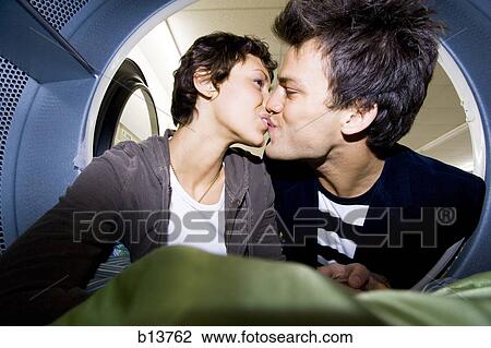 Stock Image - Couple kissing inside dryer at Laundromat with clothing. Fotosearch