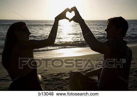 Couple on a beach making a heart symbol with their hands View Large Photo Image Stock Photo - Couple on a beach making a heart symbol with their hands. Fotosearch