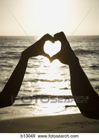 Stock Photo - Couple on a beach making a heart symbol with their hands. Fotosearch