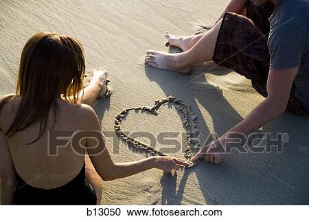 Couple on beach drawing valentines in sand View Large Photo Image Stock Image - Couple on beach drawing valentines in sand. Fotosearch