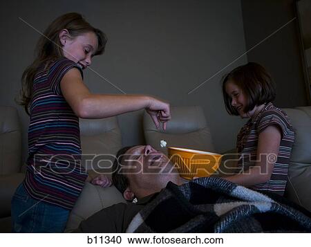 Daughters dropping popcorn into sleeping father's mouth View Large Photo Image Stock Image - Daughters dropping popcorn into sleeping father's mouth. Fotosearch