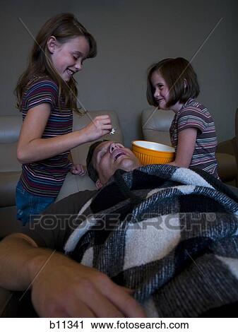 Daughters dropping popcorn into sleeping father's mouth View Large Photo Image Stock Image - Daughters dropping popcorn into sleeping father's mouth. Fotosearch