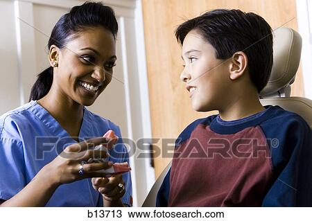 Dental hygienist holding false teeth talking to boy View Large Photo Image Stock Image - Dental hygienist holding false teeth talking to boy. Fotosearch